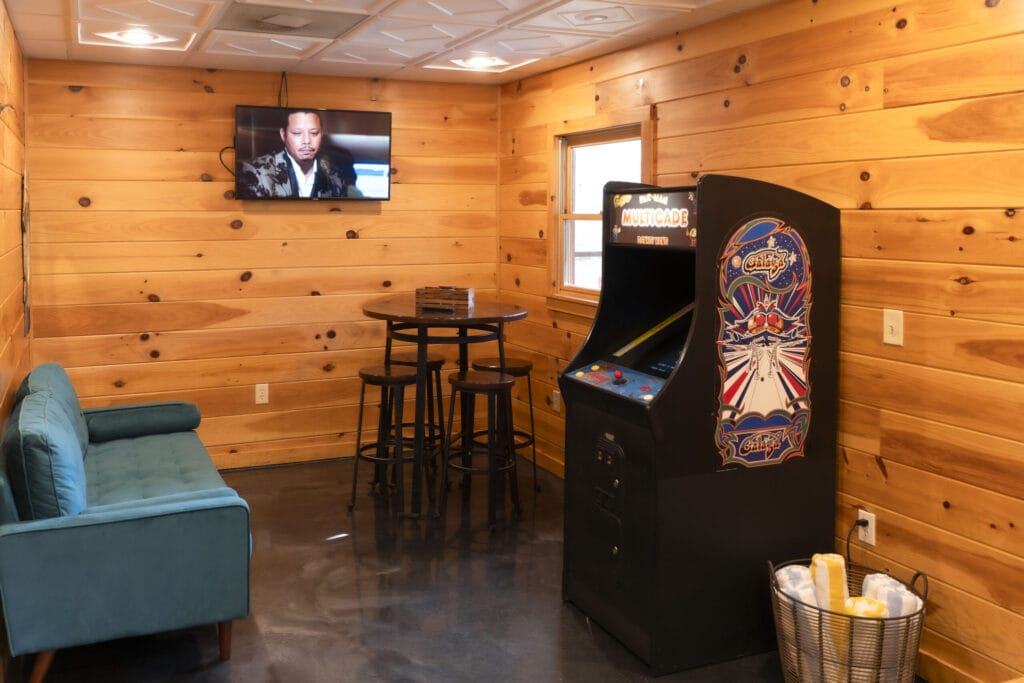 Game room of the Lincoln Logs Cabin with towels, an arcade machine, a sofa, a tall table, and a television